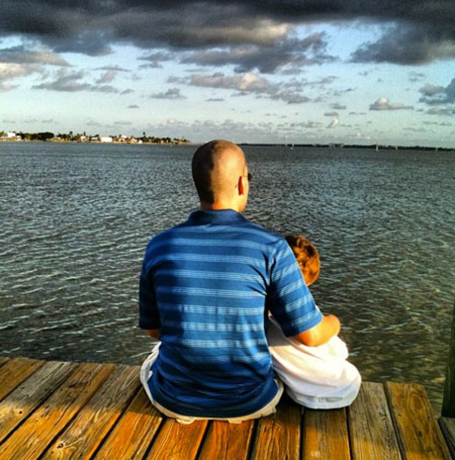 man with his arm around young boy sitting on a dock