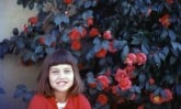 young smiling girl next to a large bush