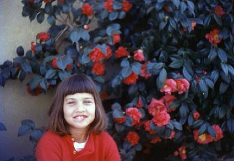 young smiling girl next to a large bush