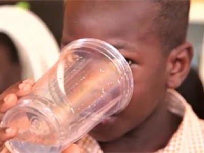 a child in a yellow and white shirt drinking a glass of water