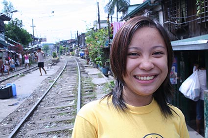 smiling young woman standing next to railroad tracks