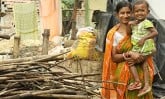 Mother holding her daughter by a wood pile outside their home in India