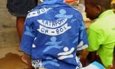Back of a child wearing a blue uniform shirt with a center number and skippy image