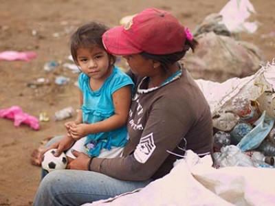 litle girl in a blue shirt sitting next to a woman wearing a red baseball cap