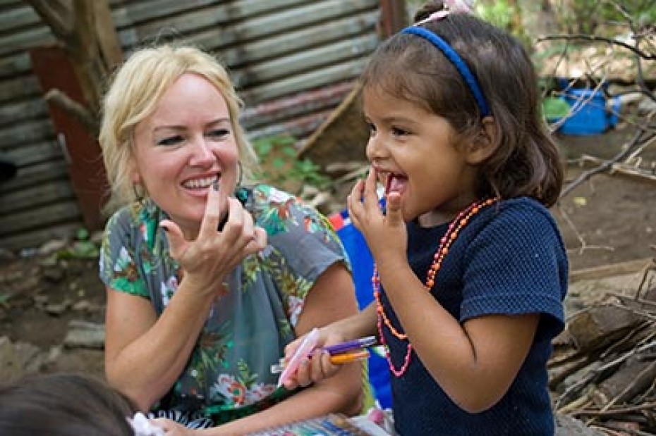 A women in a blue flowered blouse sitting next to a little girl wearing a blue shirt both touching their mouths with their hands