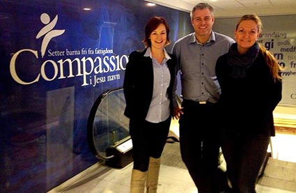 Two ladies and a man standing in front of a Compassion banner.