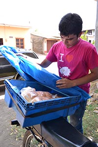 young man placing baked goods in container on back of motorbike