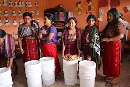 Several women standing behind small stacks of white buckets