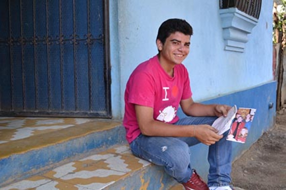 boy in a red shirt and denim pants sitting on a step holding a piece of paper