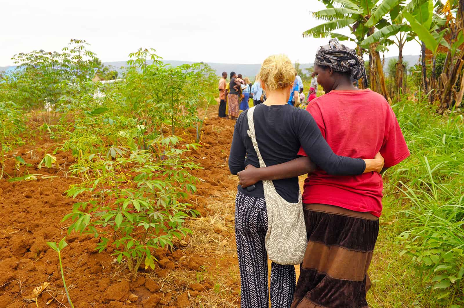 Two women walk down a dirt path together with their arms around one another.