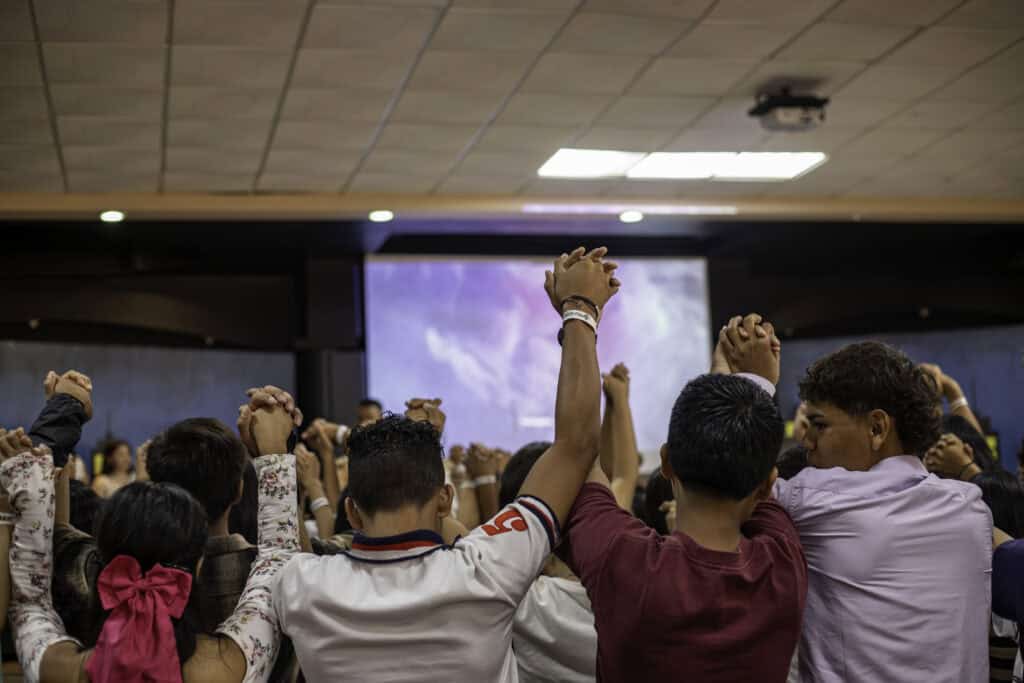  A group of teenagers hold hands in the air with their backs turned.