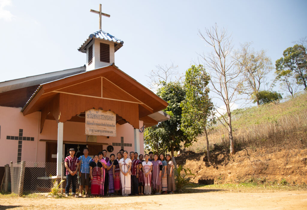 A group of men and women stand outside of a church while smiling for the camera.