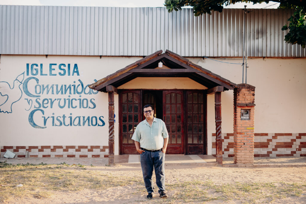 An older man stands outside of a building and smiles for the camera.