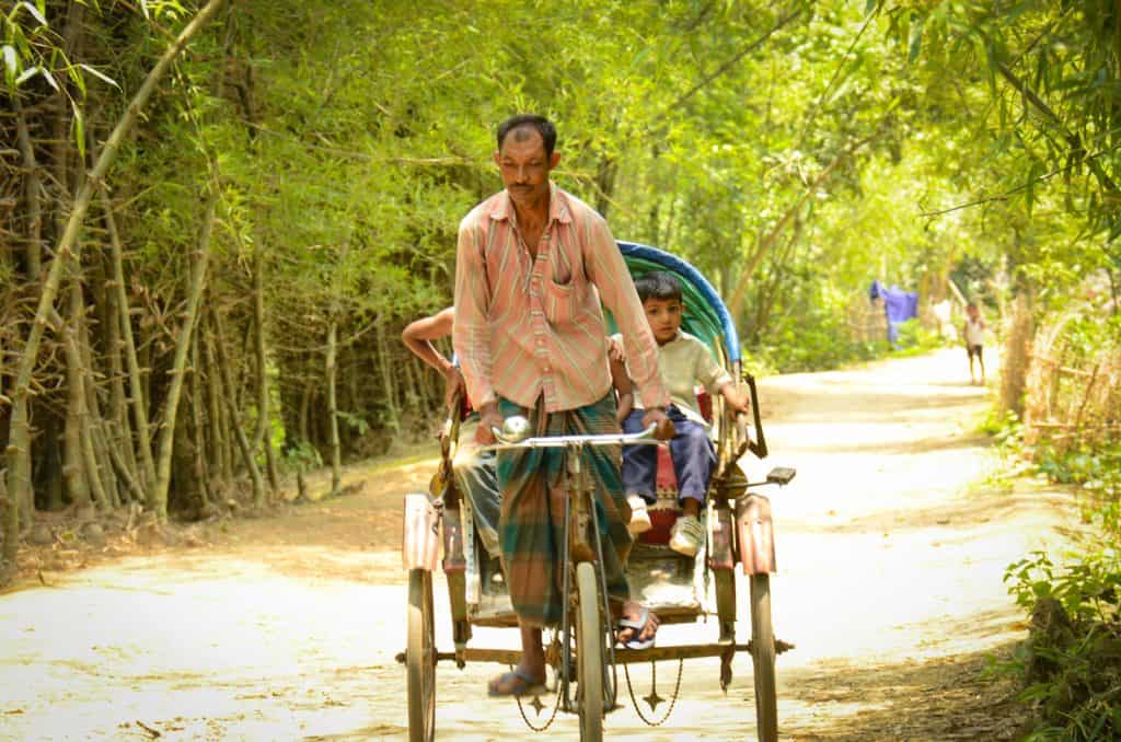 A man drives a rickshaw with children riding on it