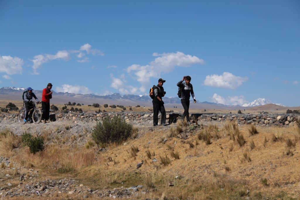 Students in Bolivia hike on rough terrain on their journey to school. They are on the plains, and mountains are in the distance.