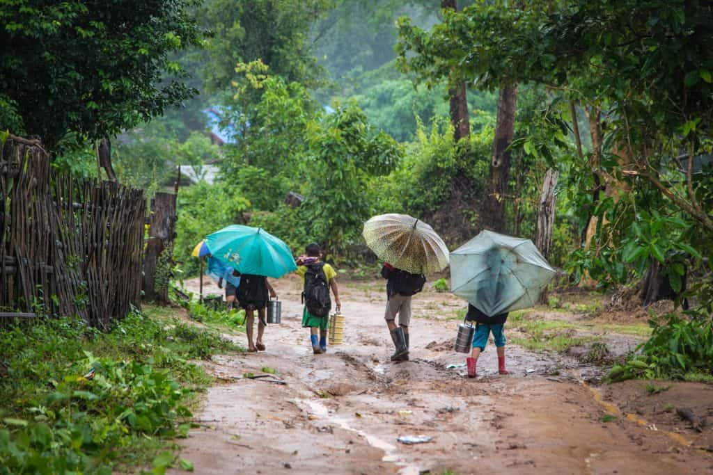Children holding umbrellas walk through the rain and mud in Thailand