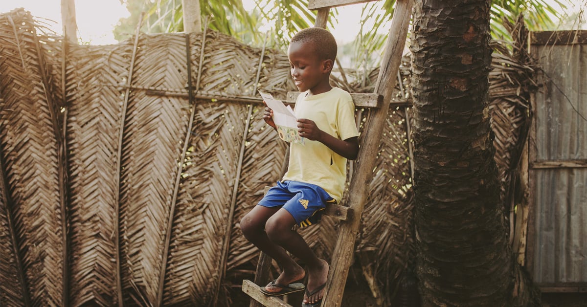 Young boy in a yellow shirt sitting on a step ladder reading a letter