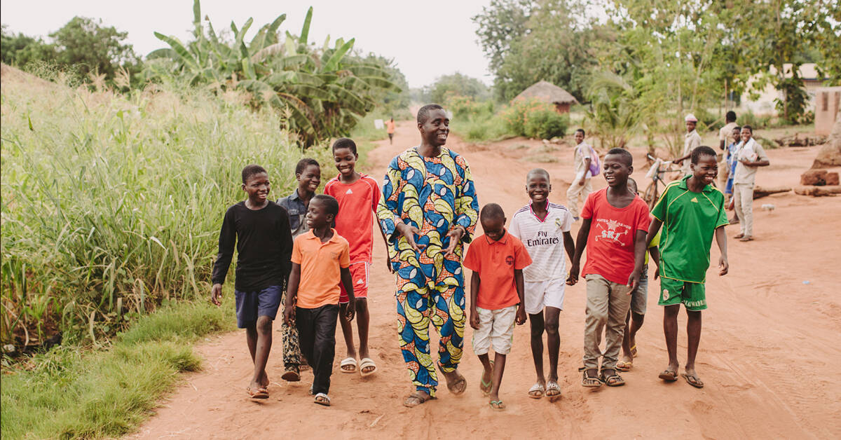 man walking along dirt road surrounded by children