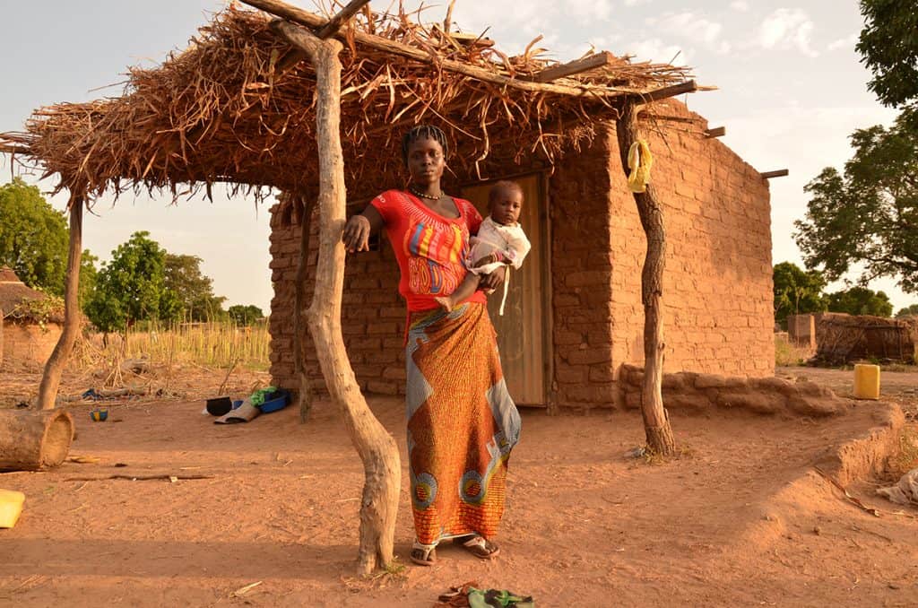 A mother holds her child outside their tiny home in Burkina Faso