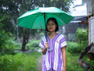 A girl in Thailand stands under an umbrella in the rain