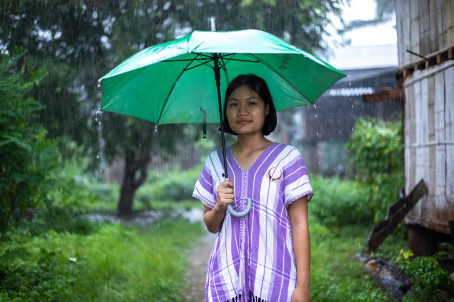 A girl in Thailand stands under an umbrella in the rain