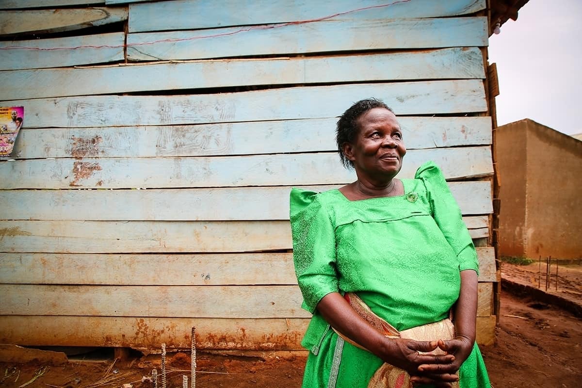 Betty, a local Ugandan village leader, stands outside wearing a green dress and smiling