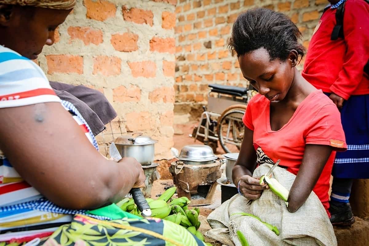 Grace peels fruit, preparing to cook a meal outside her home in Uganda