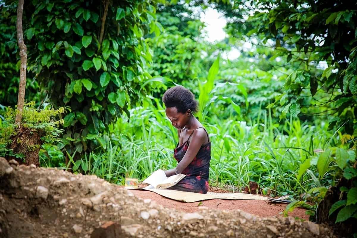 Grace sits on a mat on the ground outside, reading a book