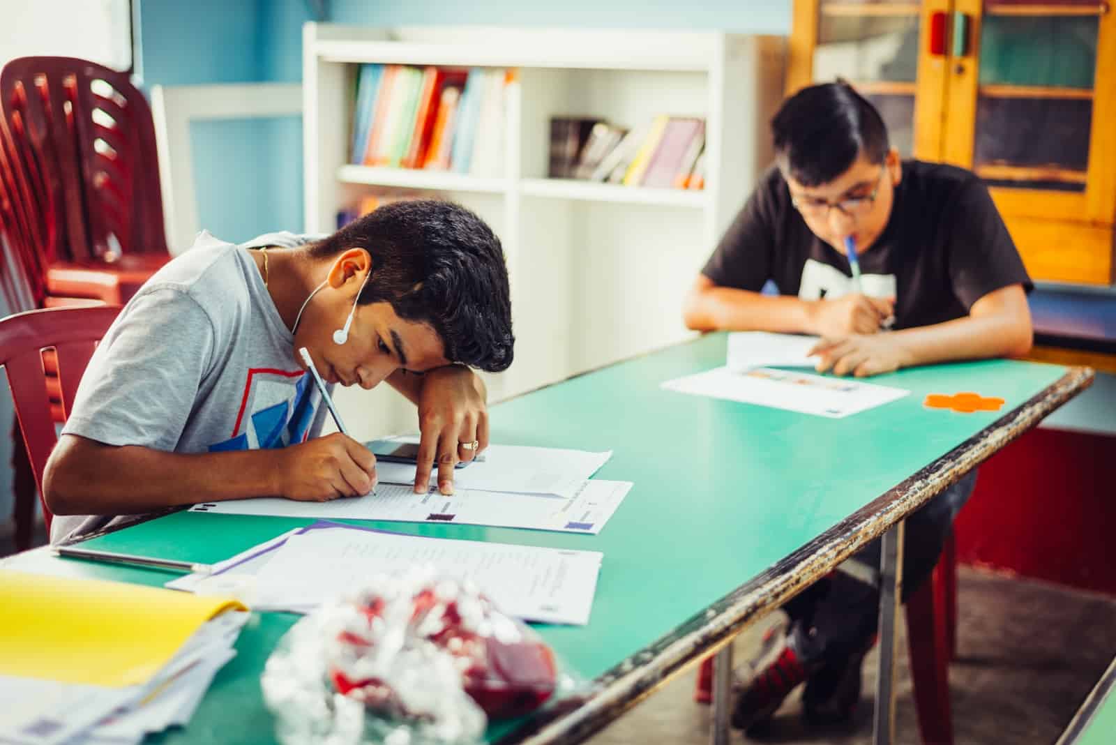 two young men sitting at a table writing letters