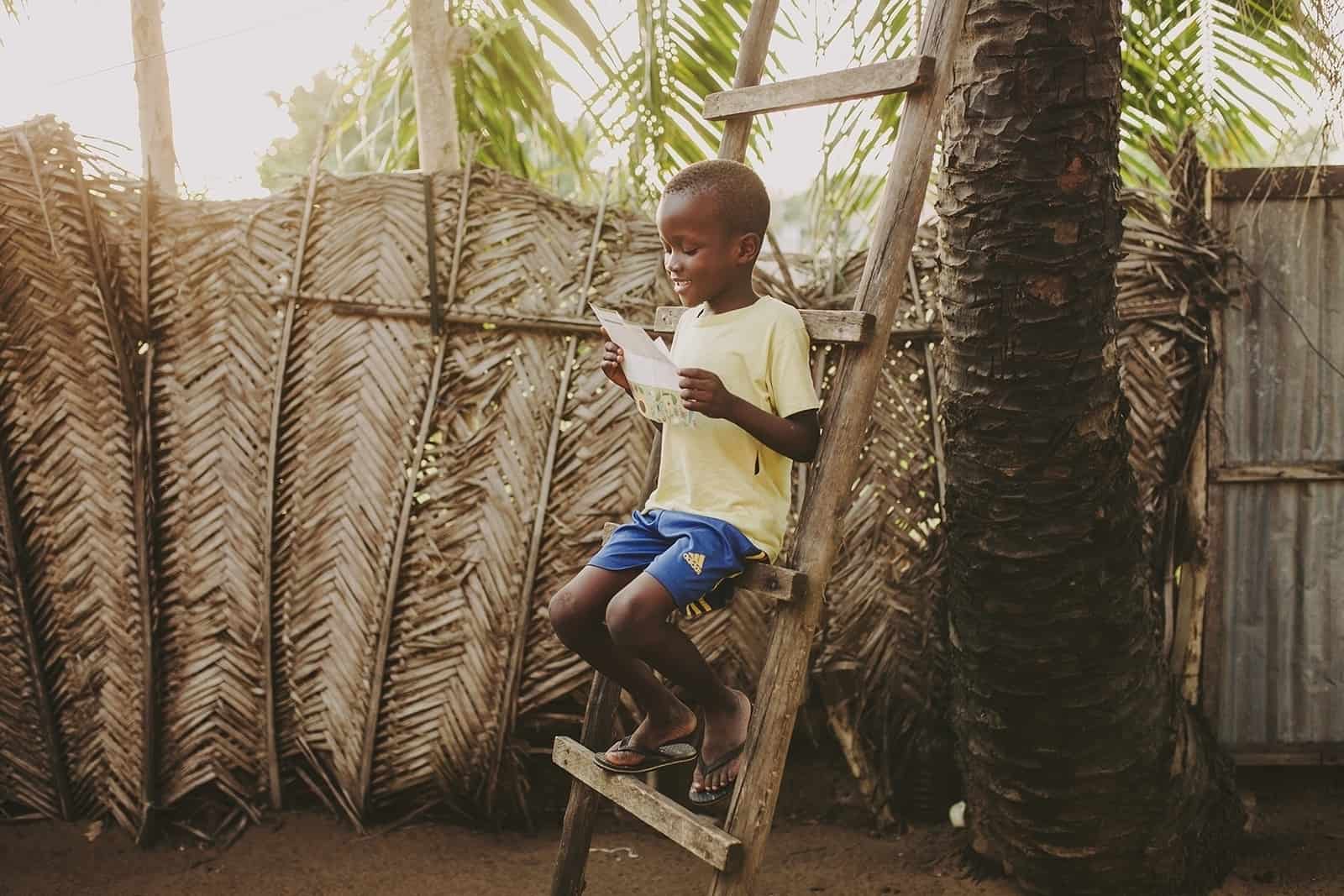 young boy sitting on a wooden ladder reading a letter