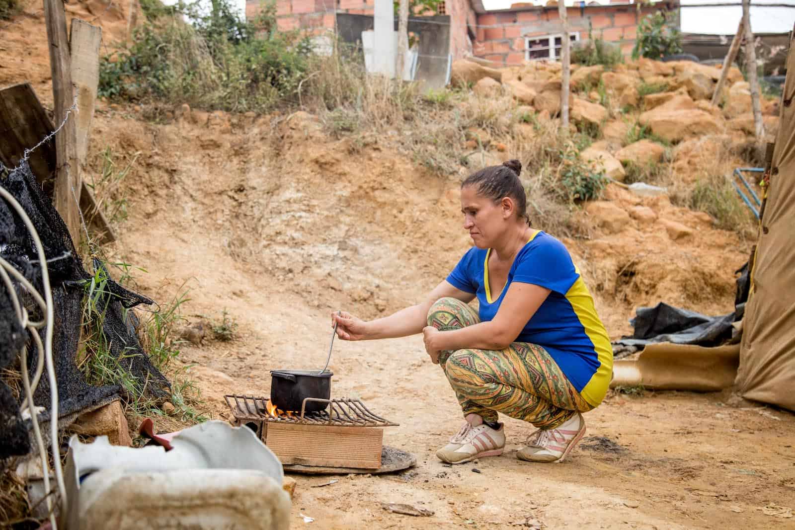 A woman crouches outside cooking on a fire.