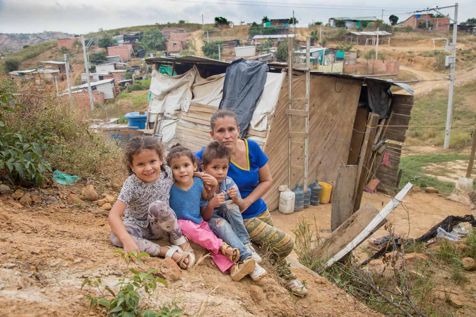 A woman and three children sit outside of a one-room home made of wood and plastic tarps where they are housing people who have left Venezuela after the political crisis.