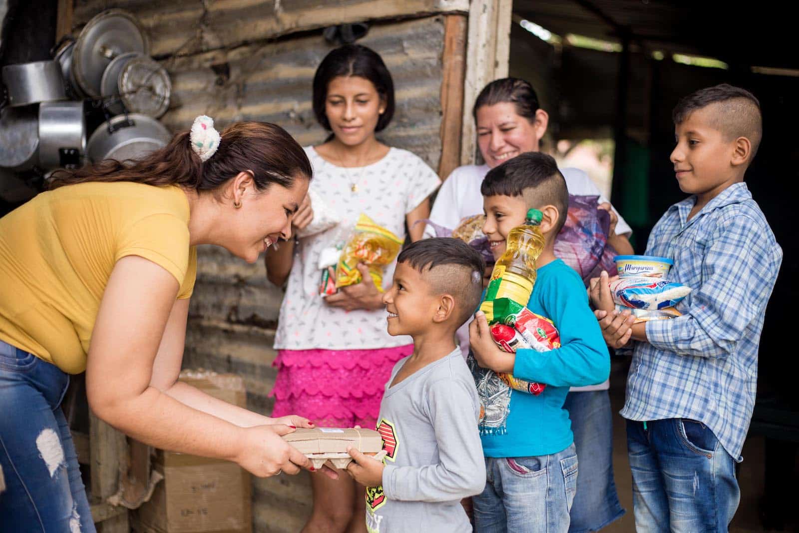 A woman leans over, handing groceries to a boy whose family has been feeding Venezuelans who fled to Colombia out of hunger.