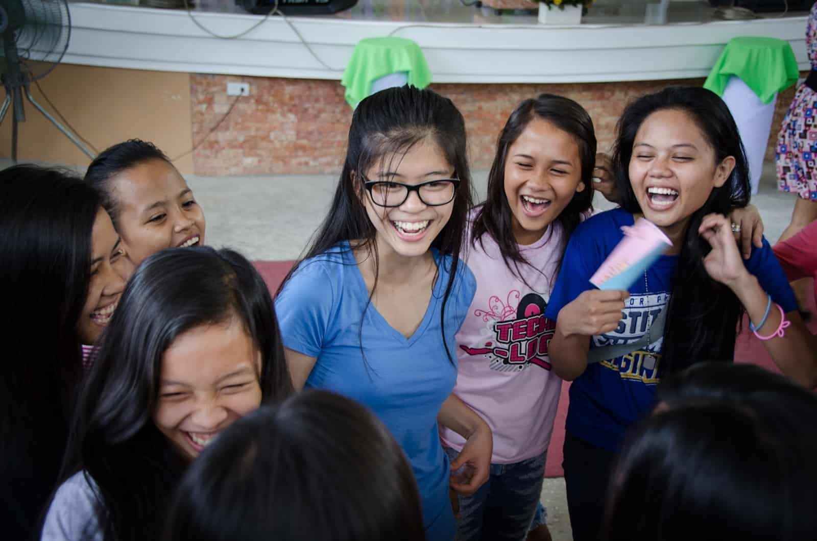 A group of girls smiles and laughs, standing inside a church. 