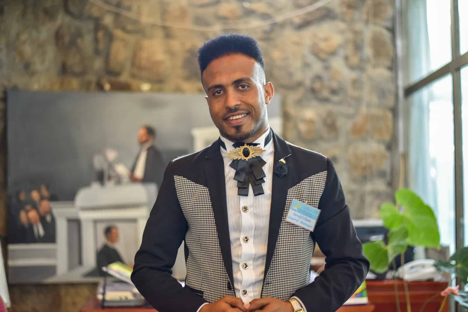 A man stands in a hotel lobby wearing a black, white and gray suit.