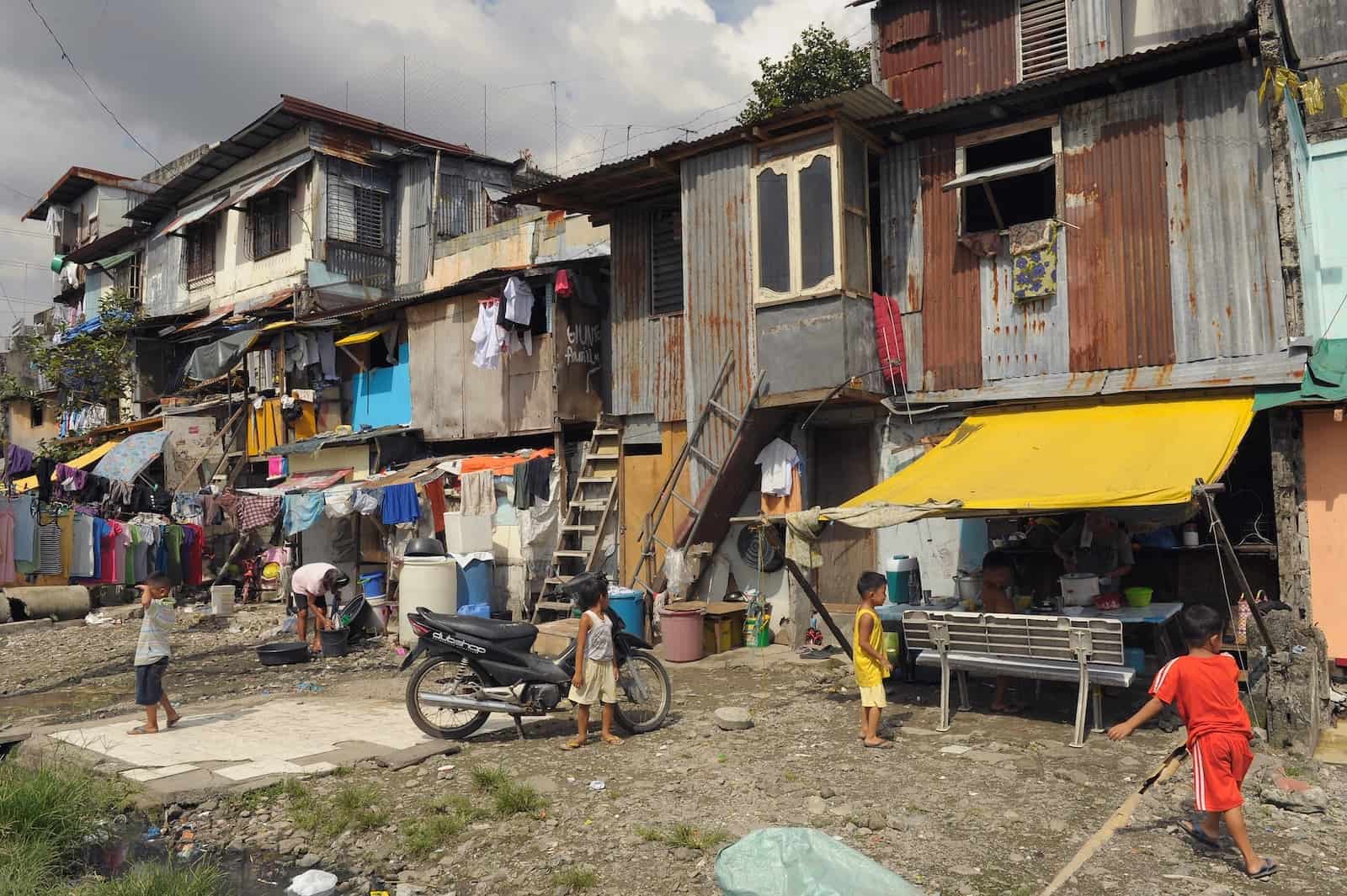 A row of makeshift homes on a street, several stories high, made from metal sheets and wood, showing poverty in Asia.