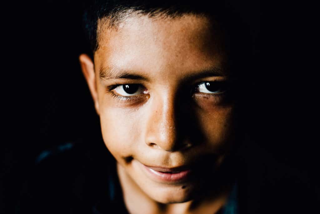 A close-up of a young boy smiling at the camera in front of a black background.