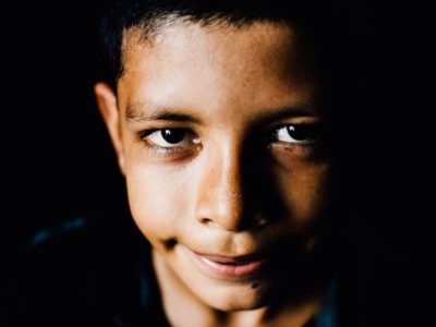 A close-up of a young boy smiling at the camera in front of a black background.