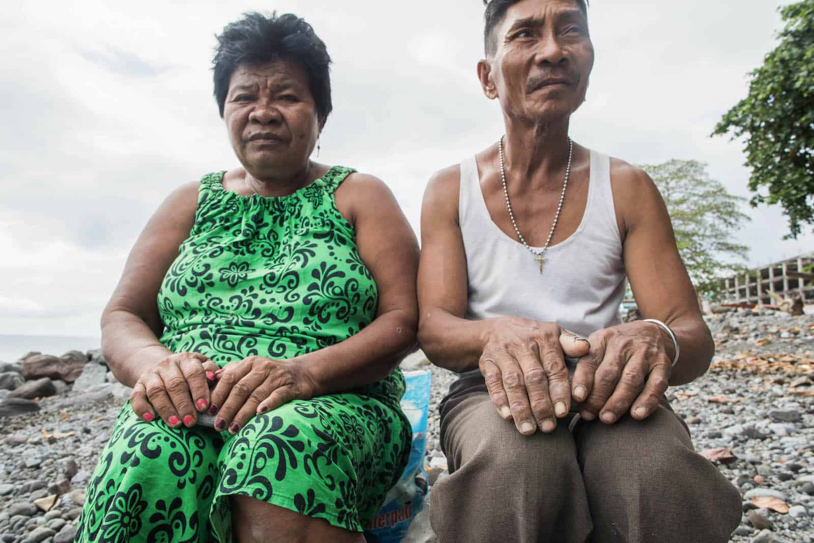 A man and women sit on a beach, with their hands on their laps.