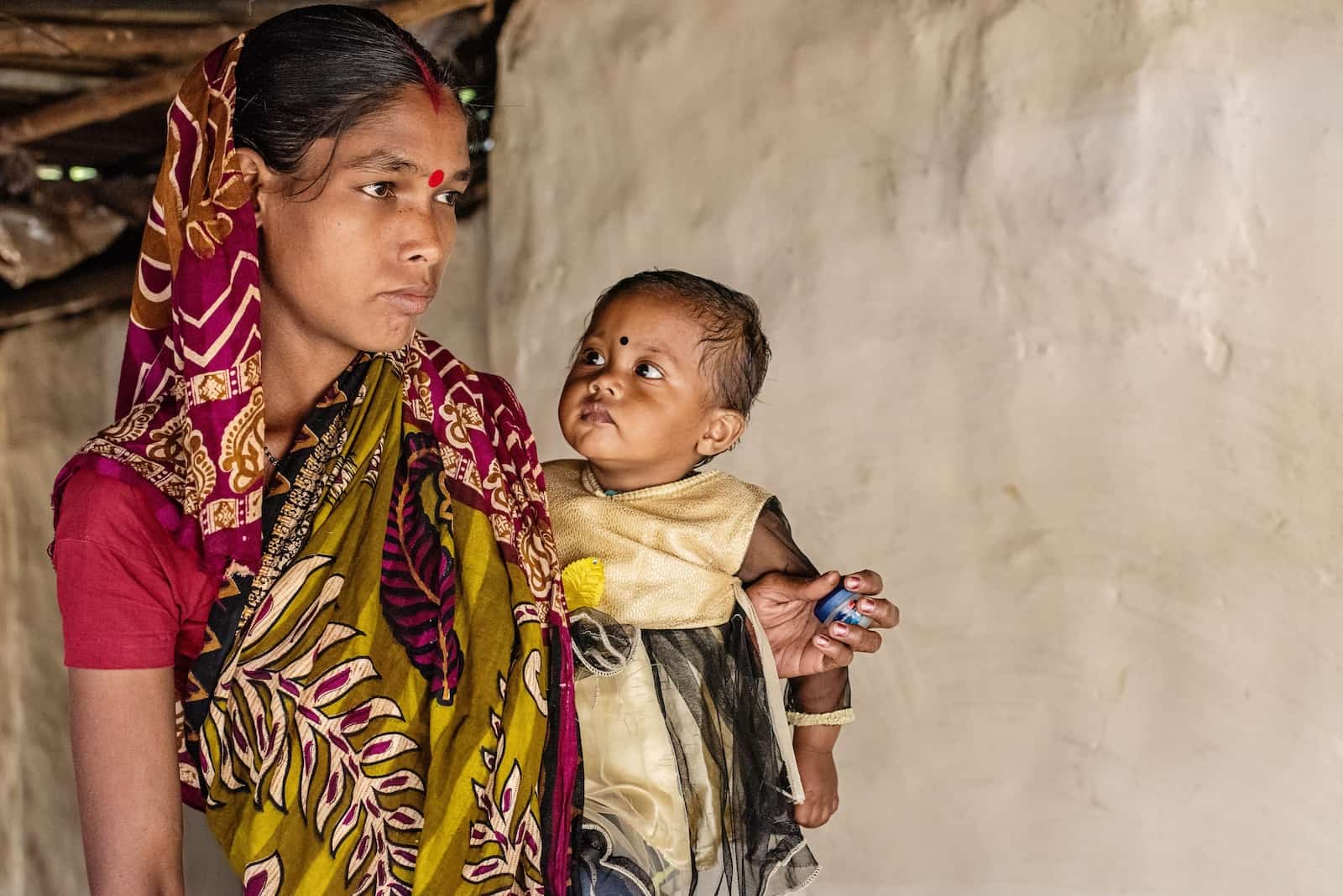 A woman in a colorful sari with a red bindi on her forehead holds a baby girl, who is looking at her. Report: Hunger Is on the Rise Around the World