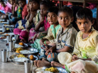 A group of children sit on the floor in a line, eating plates of rice. Report: Hunger Is on the Rise in the World