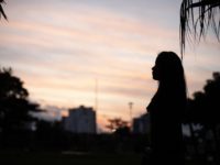A young woman is silhouetted against a dusk sky.