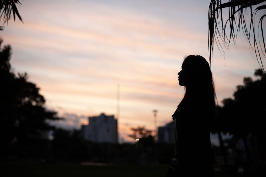 A young woman is silhouetted against a dusk sky.