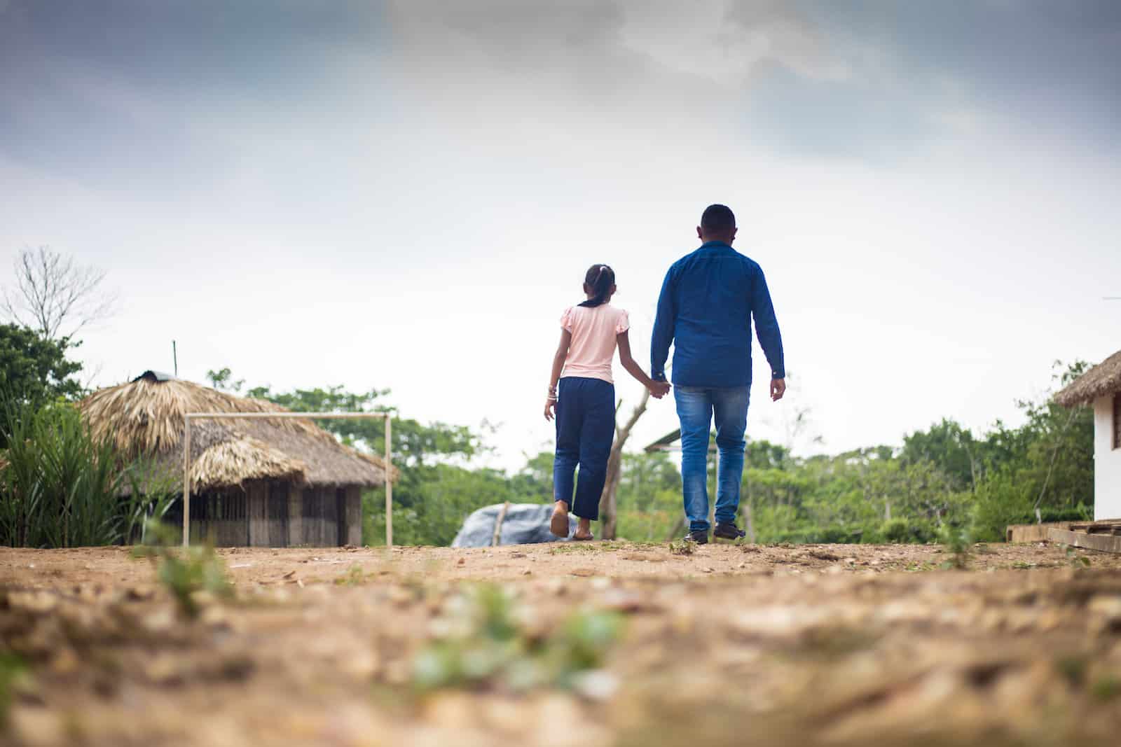 A man and girl walk down a dirt path, holding hands. 