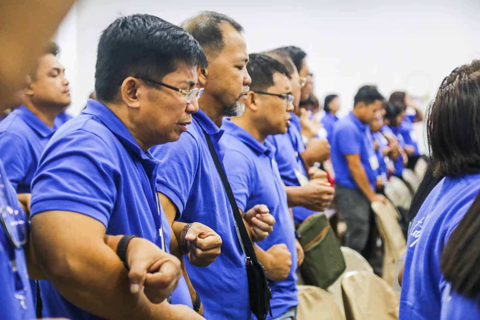A row of men in blue shirts, linking arms and praying against child sexual abuse.
