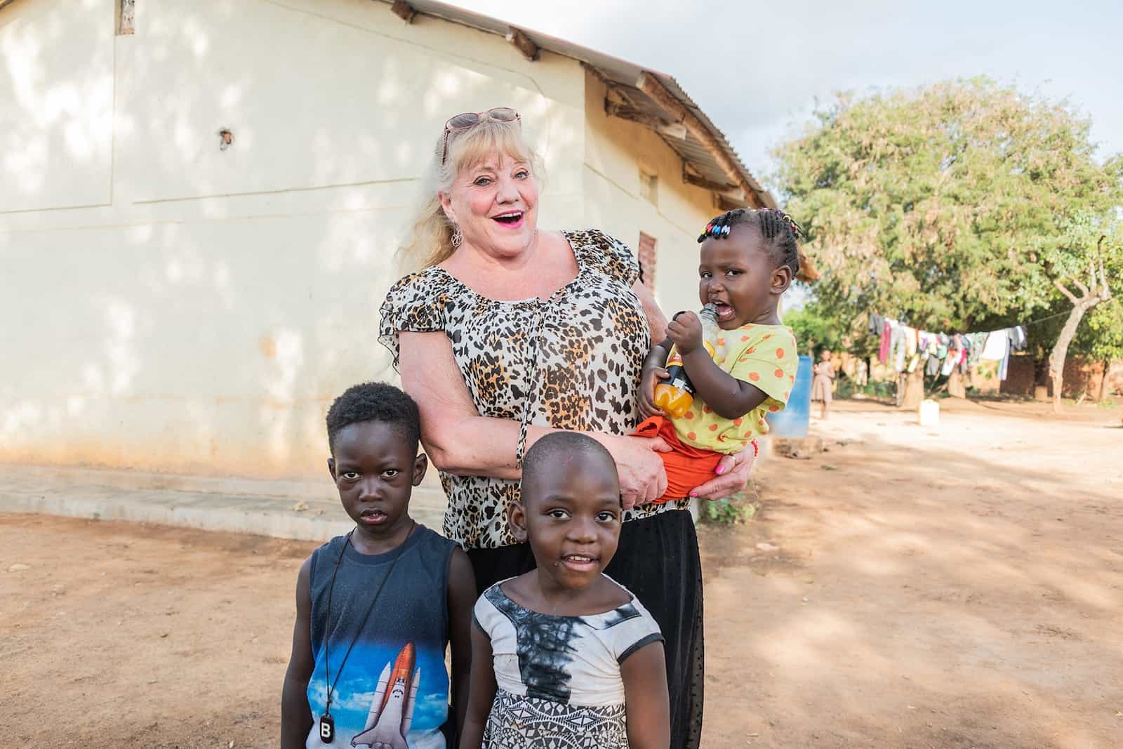 A woman stands outside holding a baby with two small children in front of her, all her namesakes. 