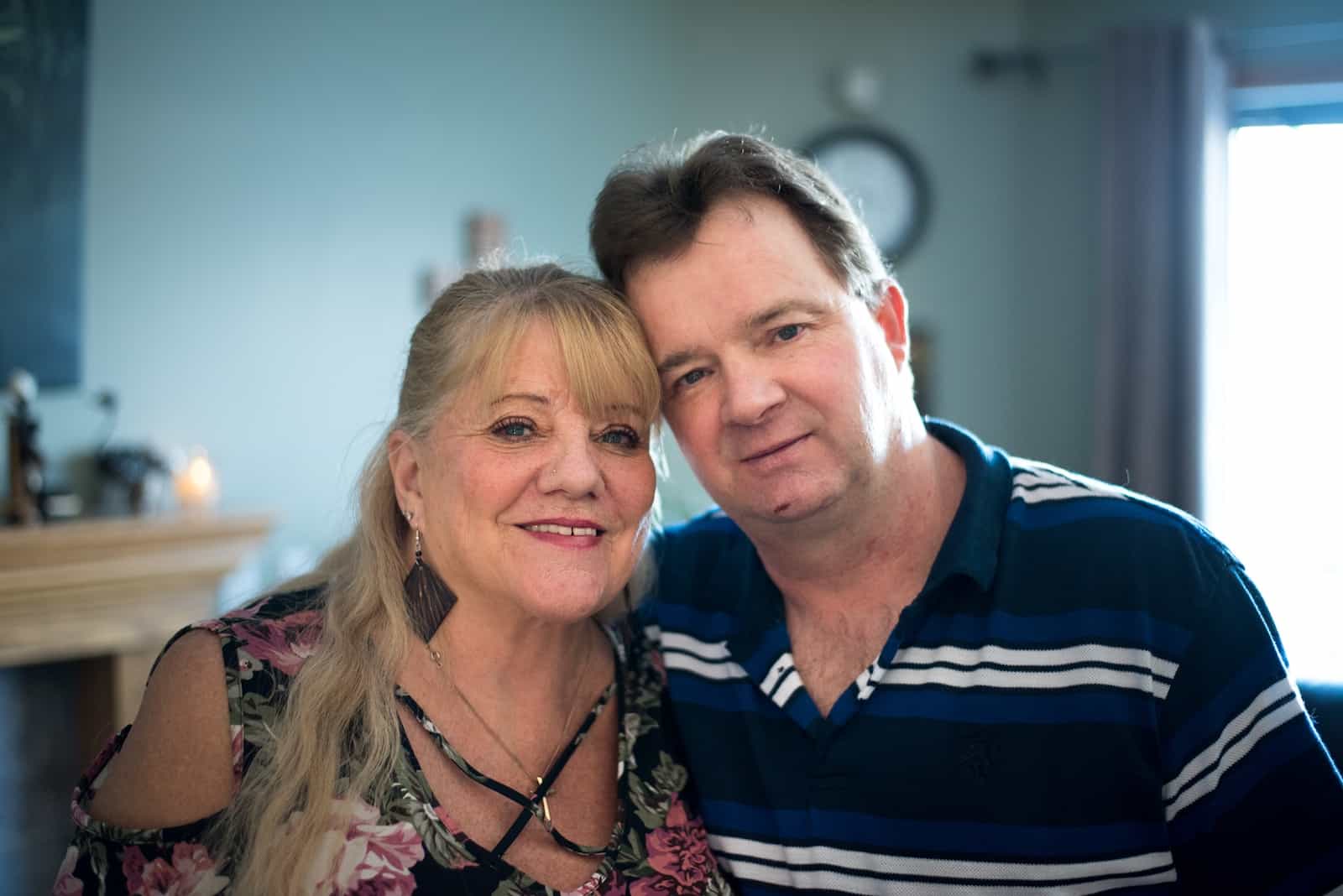 A woman in a floral shirt and a man in a black and white striped shirt pose for a photo with their arms around each other.