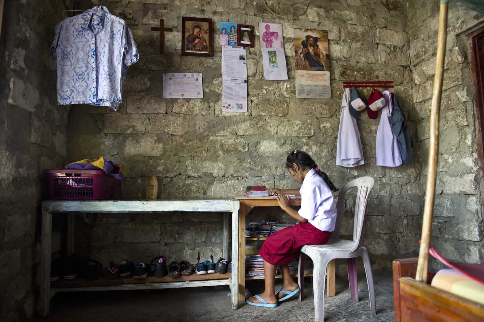 A girl sits at a desk reading a book in a brick room with pictures hung on the walls. 