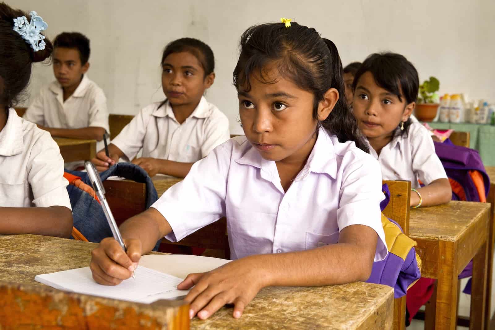 International Literacy Day: A girl sits at a desk, looking at the board in front of her, wearing a white school uniform.