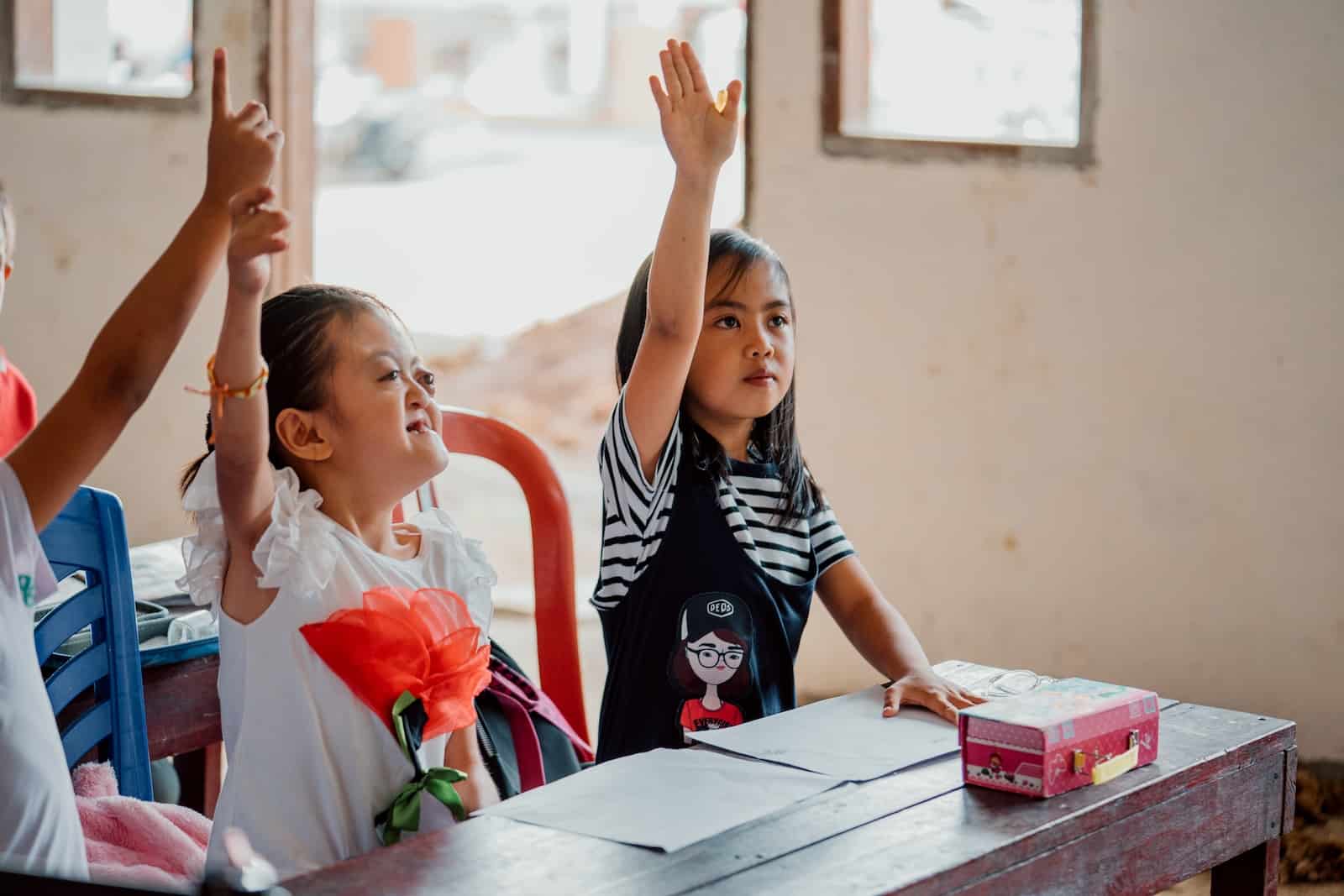 A photo of a girl with Apert Syndrome, raising her hand at school. 